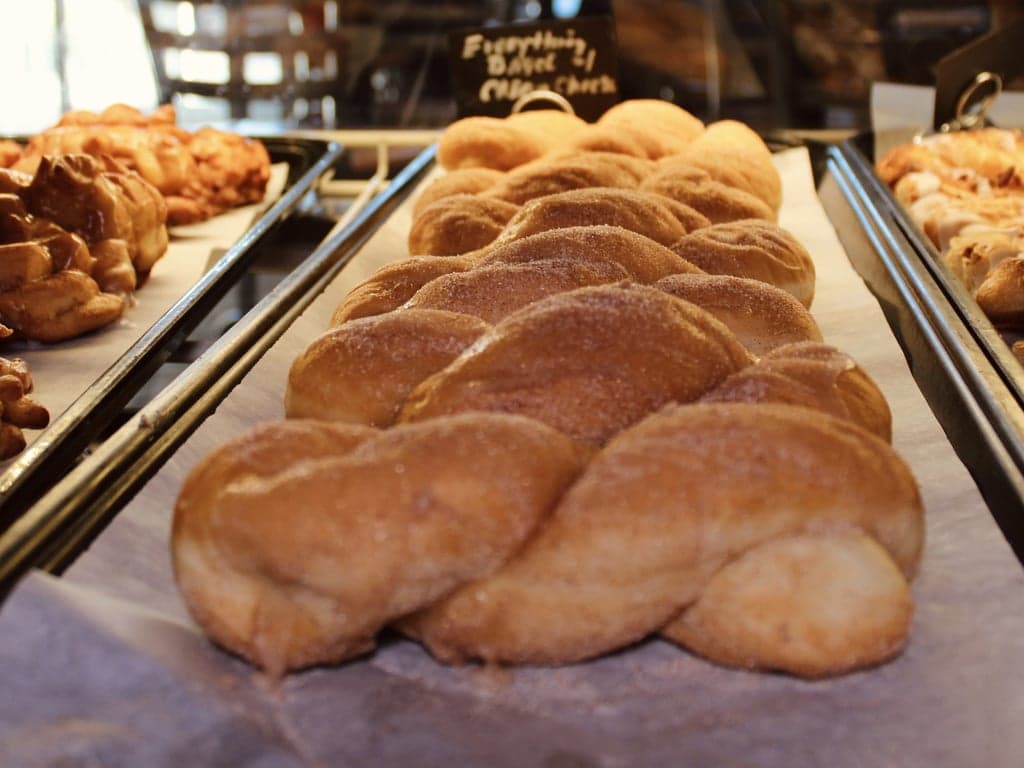 Cinnamon sugar twist donuts in the bakery case at Illinois Street Food Emporium, with apple fritters and danishes on the trays alongside.